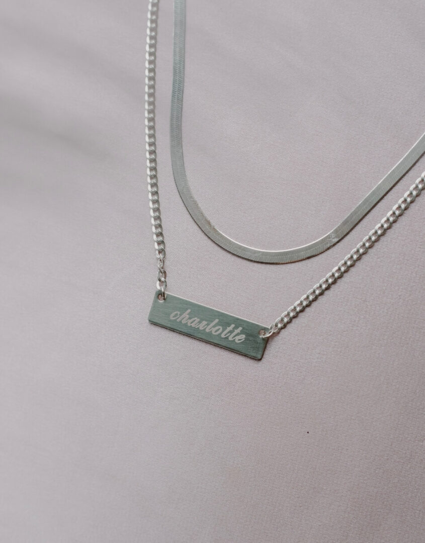 Flatlay Image of layered set of Engraved Sterling Silver Name Bar Necklace and Sterling Silver Herringbone Chain Necklace