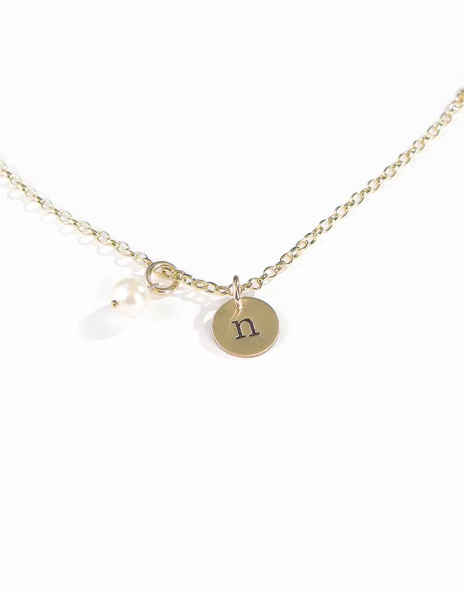 A personalized jewelry piece with hand stamped initial on the dainty gold-filled disc